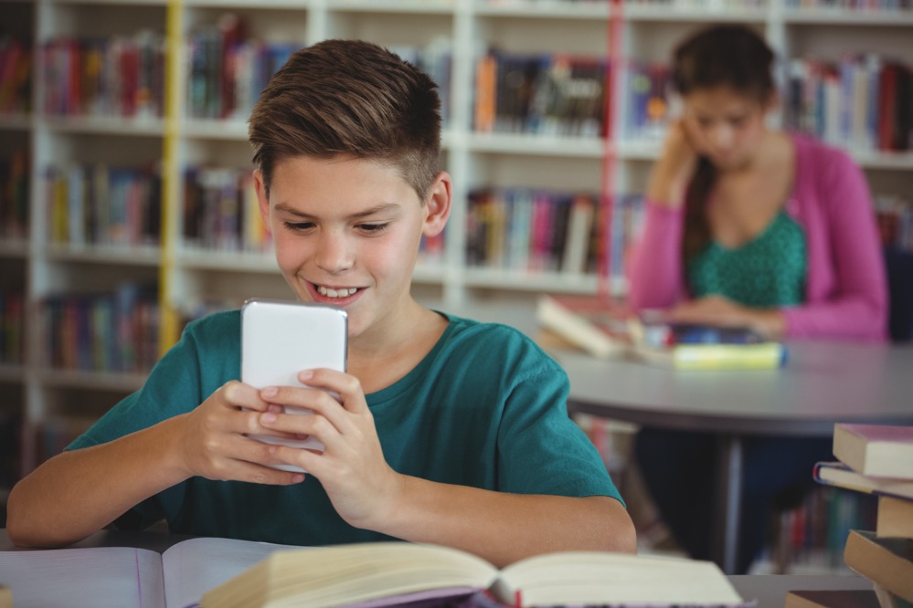 smiling-schoolboy-using-mobile-phone-library.jpg